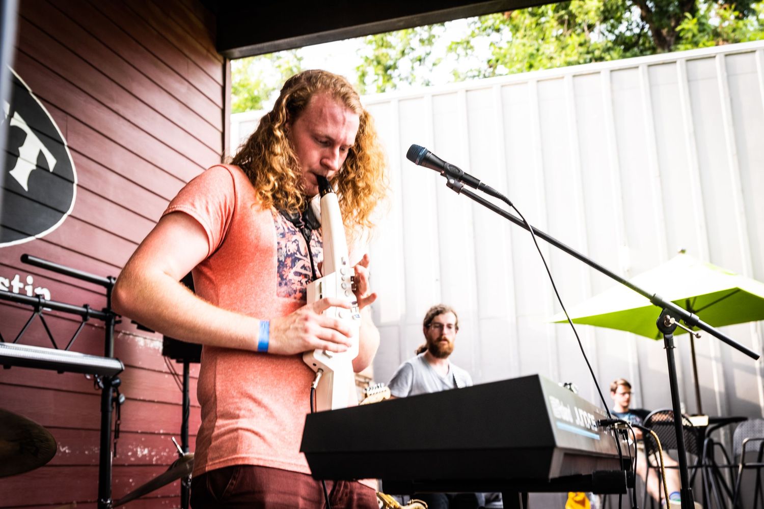 Musician in a coral t-shirt performing on stage with instruments and microphone setup.