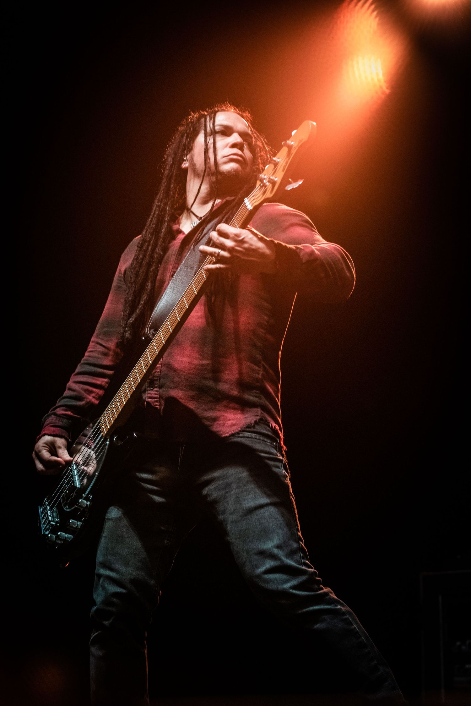 A musician with dreadlocks plays bass guitar under warm stage lighting.