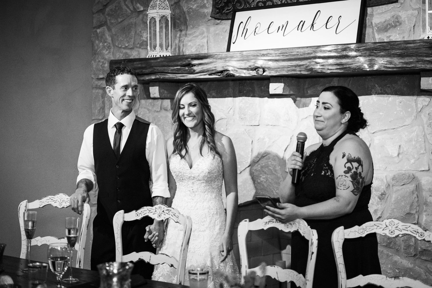 Wedding party members share a joyful moment during wedding reception speeches at a rustic venue.