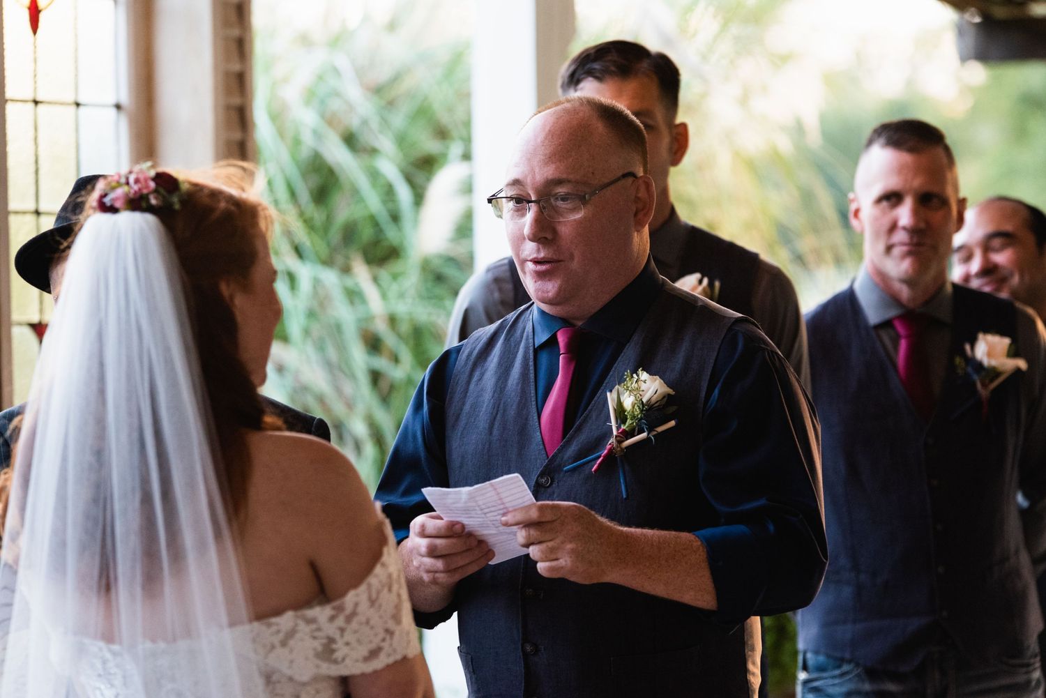 Wedding officiant reads ceremony text while attendants watch in background.