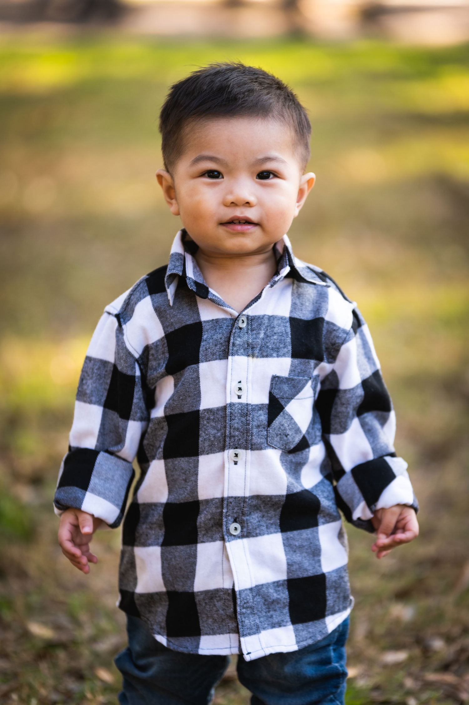 A young child wearing a black and white buffalo plaid shirt poses outdoors.