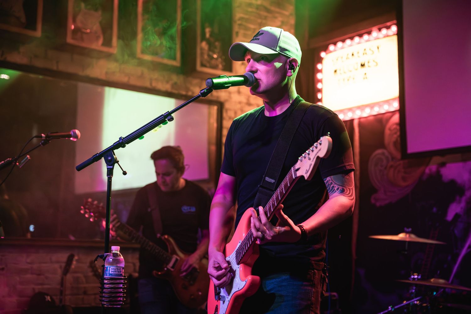 A musician performs with a bass guitar under colored stage lights at a live venue.