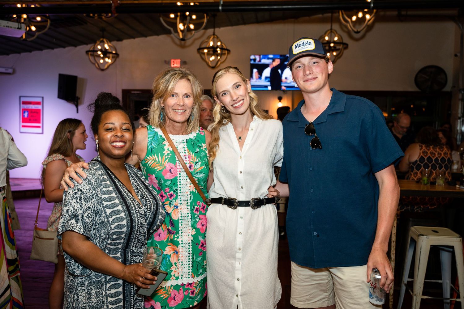 Group of four people posing together at an indoor party with decorative lighting.