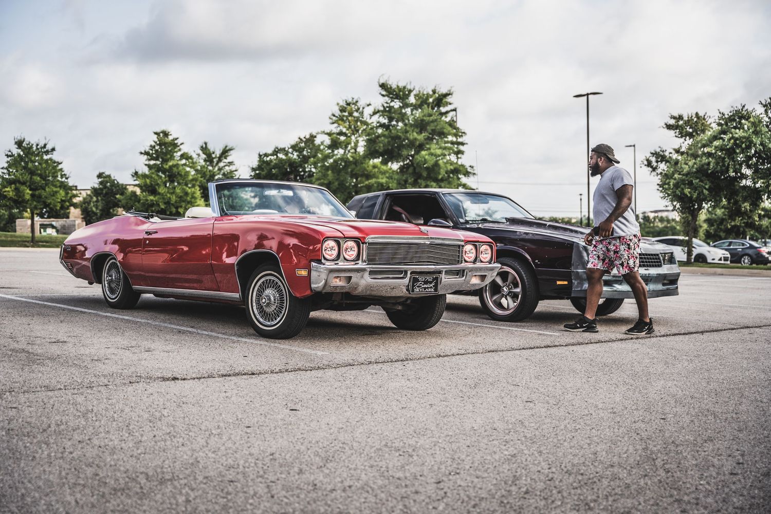 Vintage red Buick convertible and black classic car in parking lot.