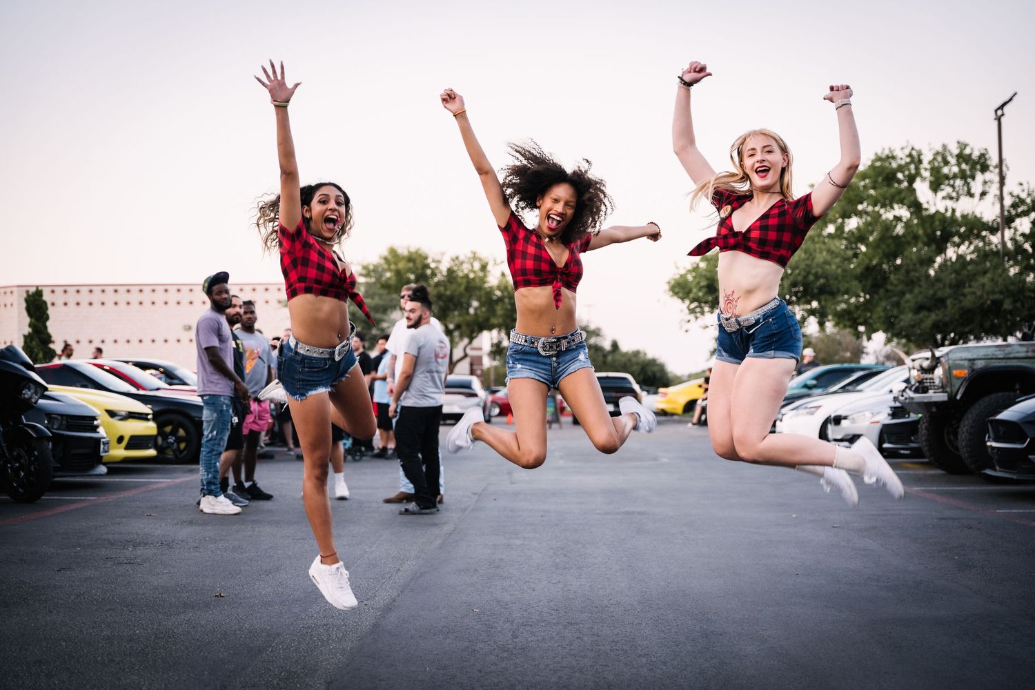 Group jumping in synchronized pose at outdoor car meet event.