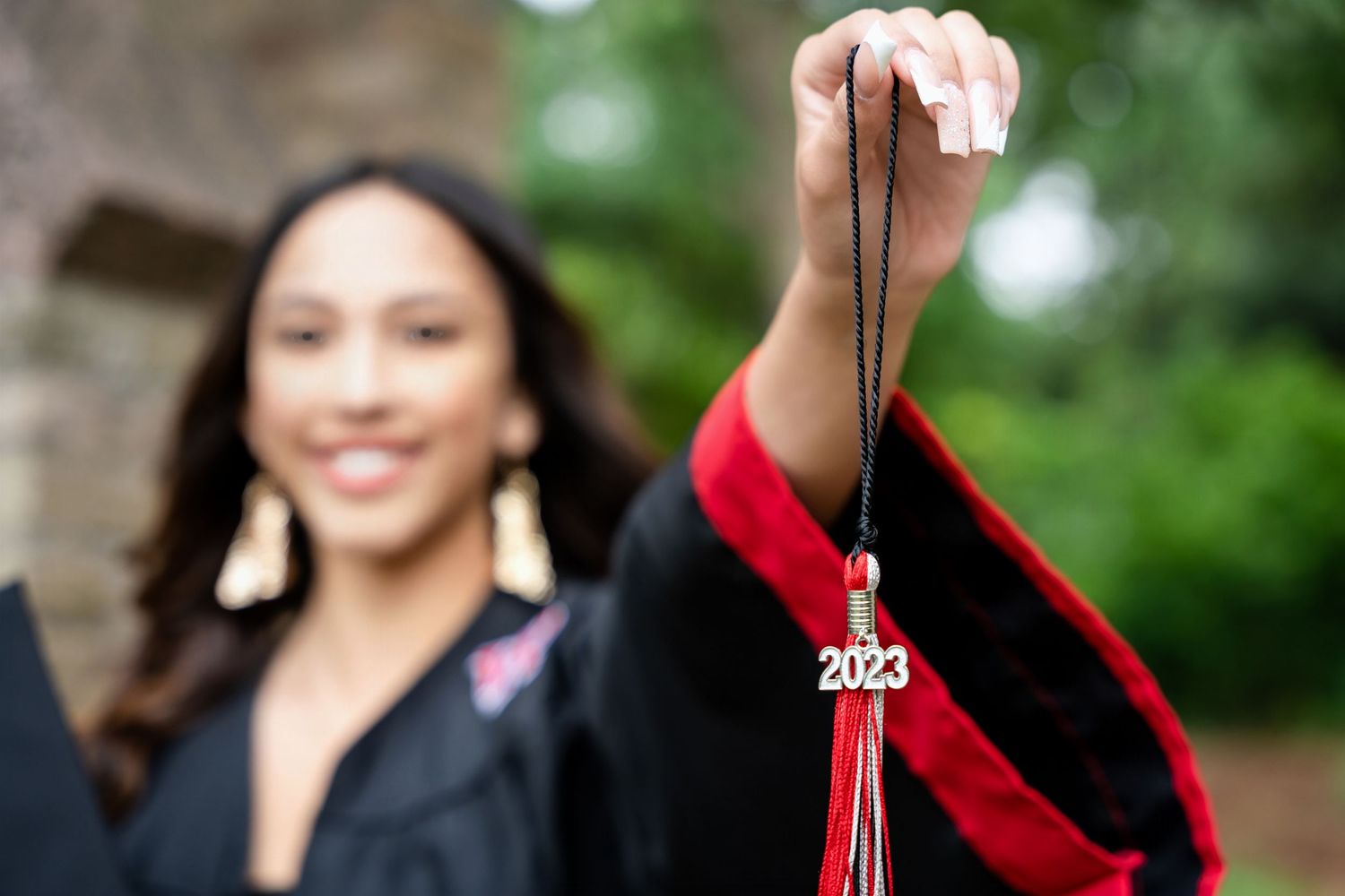 Close-up shot showing red graduation tassel and 2023 charm against blurred background.