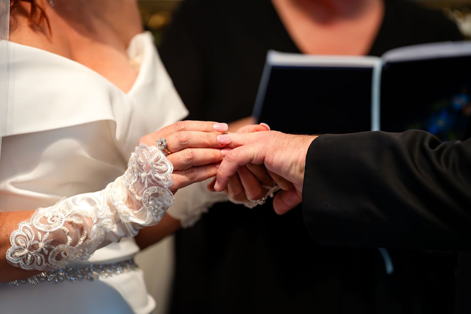 Close-up of lace-covered hands exchanging wedding rings during a ceremony.