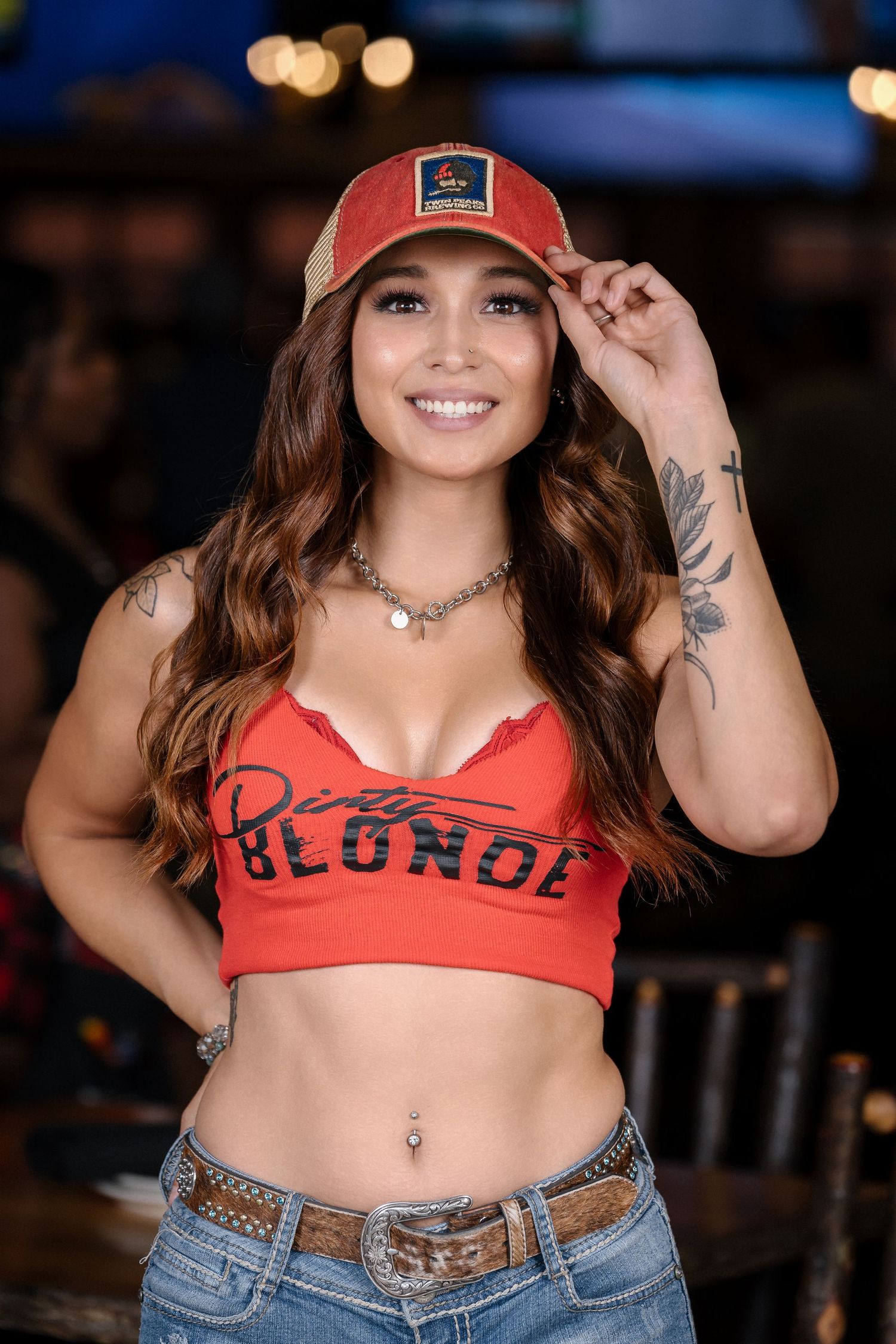 Server wearing red crop top and baseball cap poses in restaurant interior.