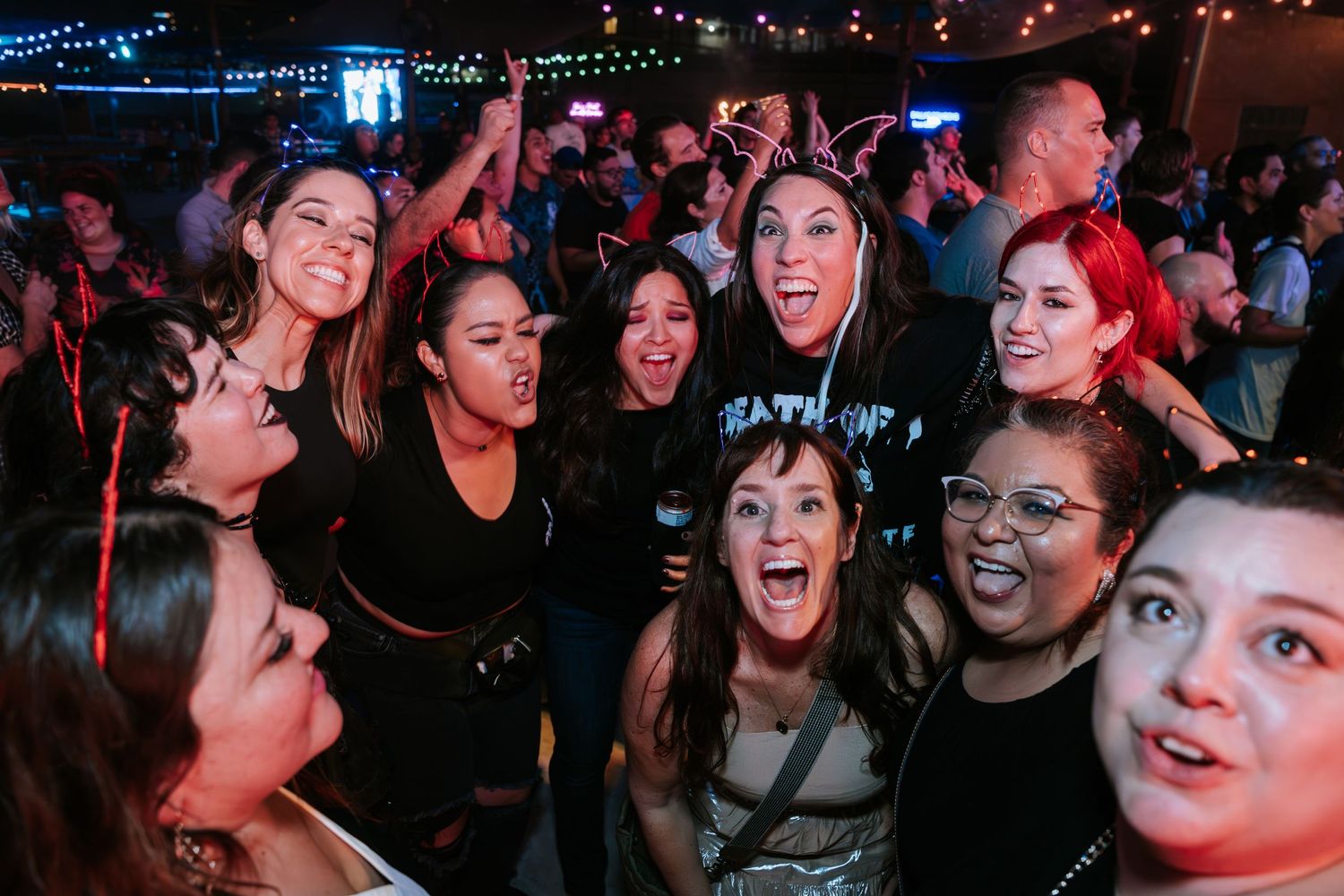 Excited crowd enjoying live music performance with colorful lighting at nightclub venue.