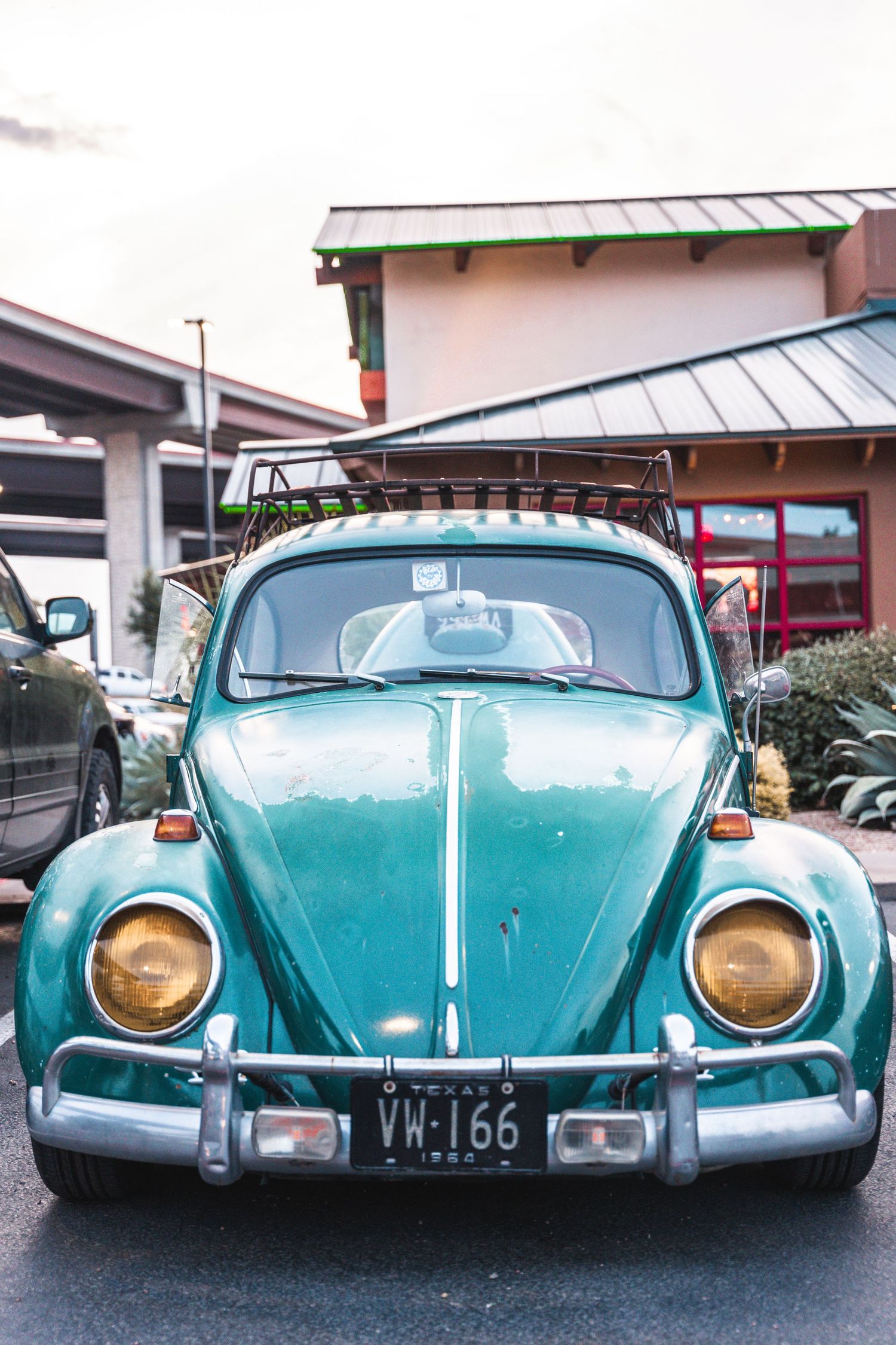 Classic turquoise Volkswagen Beetle parked in front of a retail building with distinctive round headlights.