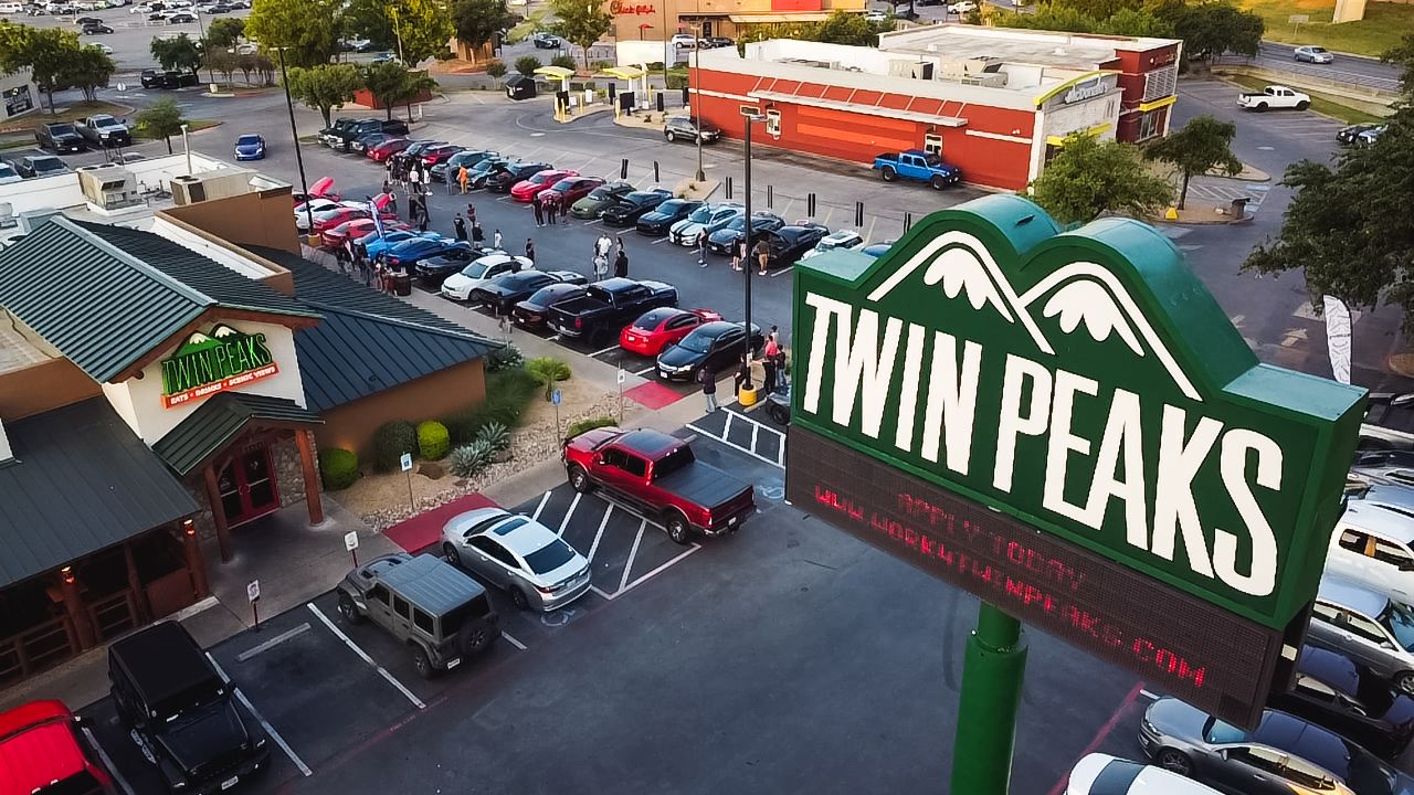 Aerial view of Twin Peaks restaurant parking lot filled with cars during a car meet event.