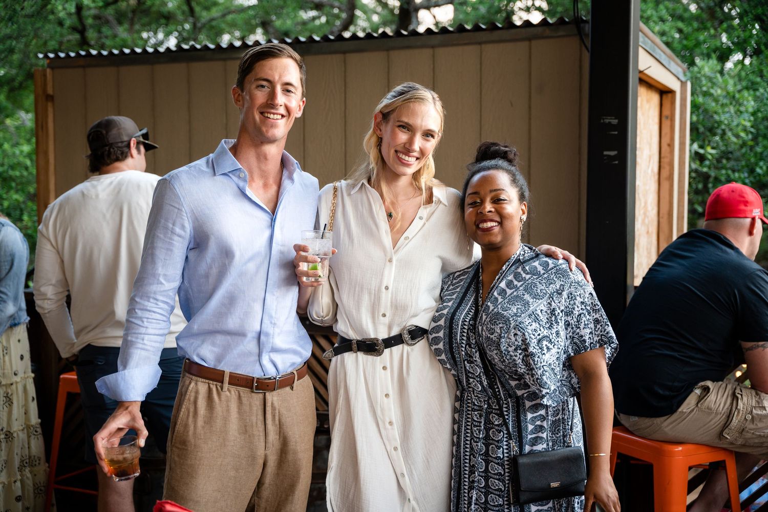 Three guests at an outdoor gathering smile and pose together at a warm social event.