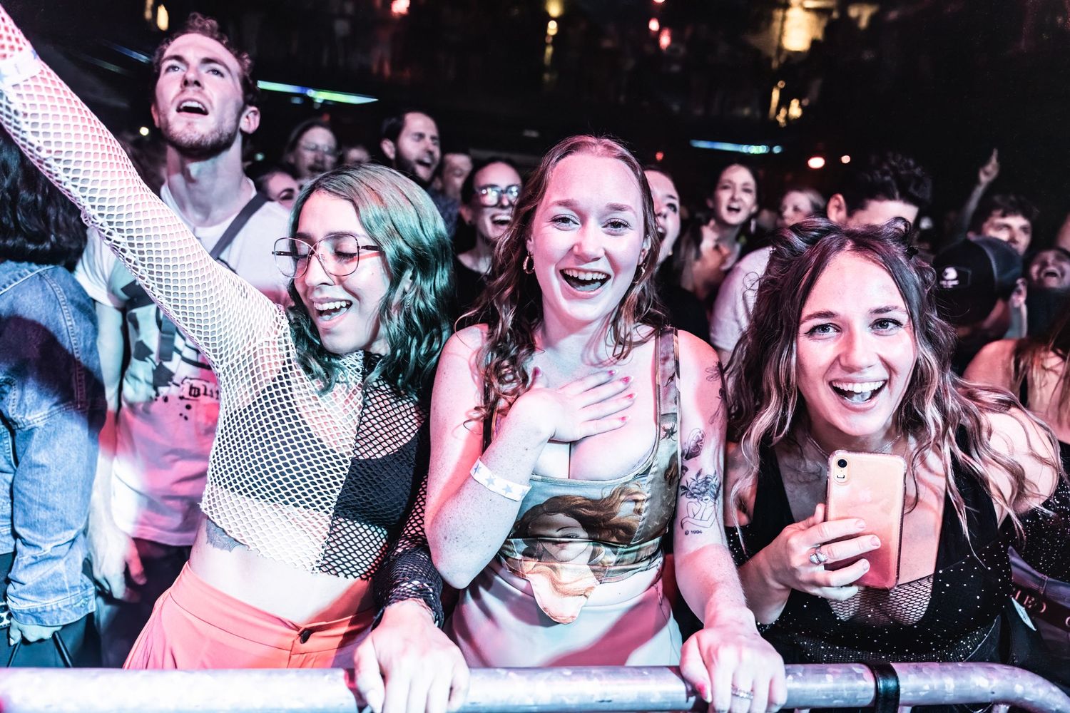 Enthusiastic fans at concert barrier react during live performance.