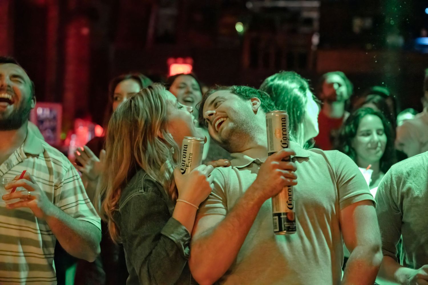 Crowd of people laughing and having fun at a nightclub under colorful red and green lighting.