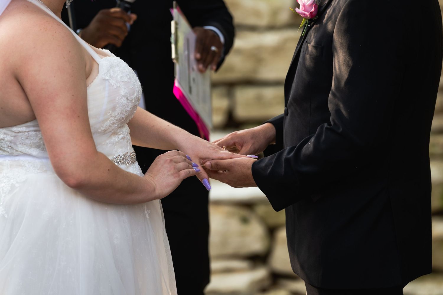Close-up shot of hands exchanging wedding rings during an outdoor ceremony.