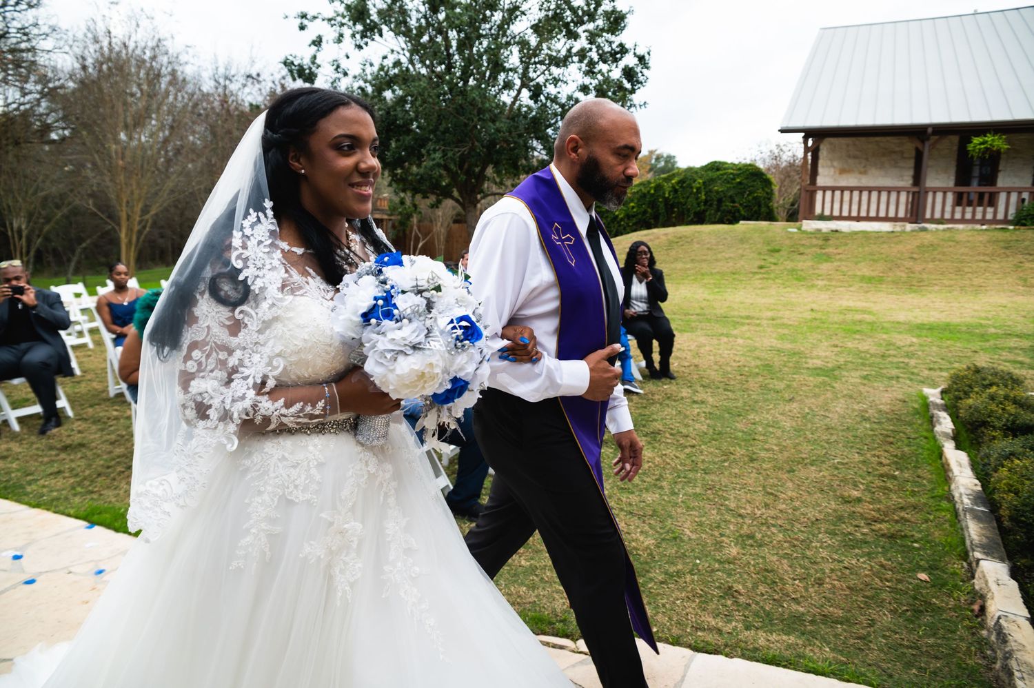 A joyful wedding procession on a grassy lawn with the officiant in purple robes.