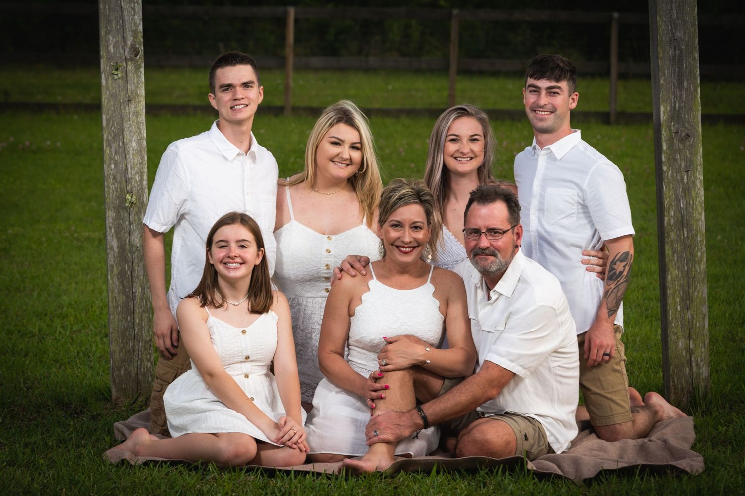 A family in coordinating white outfits poses together under a wooden arch.