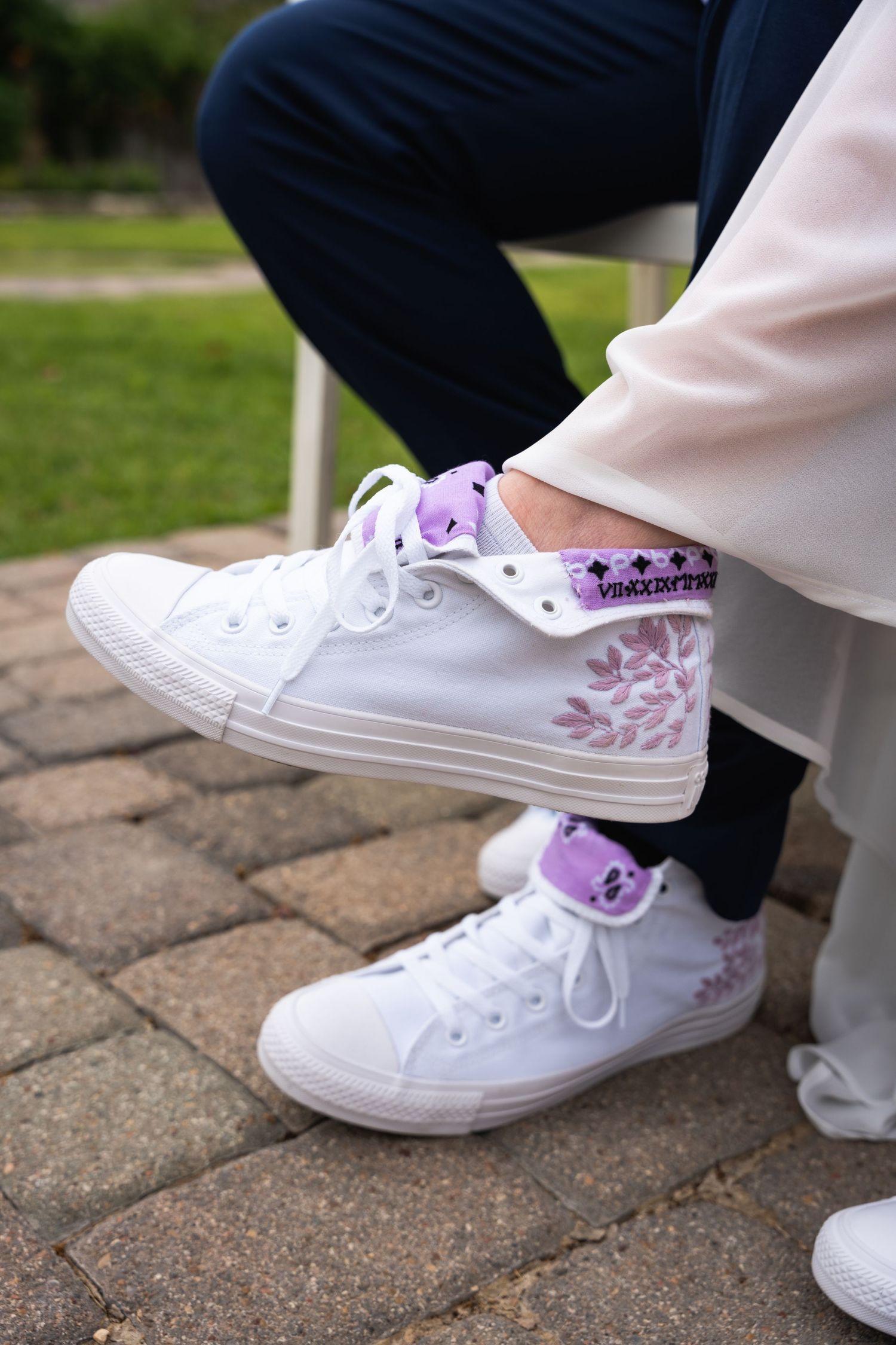 White high-top sneakers with purple floral design details on brick paving stones.