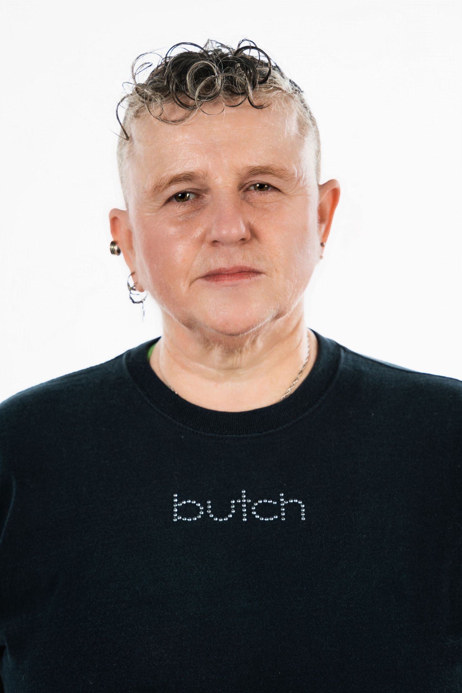 Portrait of a person with curly hair wearing a black t-shirt with 'butch' text against white background.