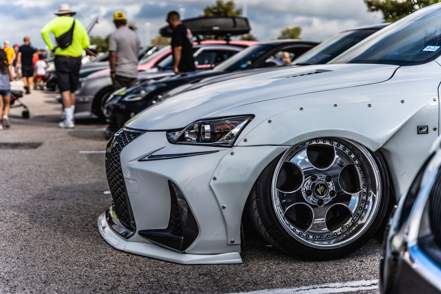 Modified white Lexus IS with aggressive fitment and chrome deep-dish wheels at a car meet.