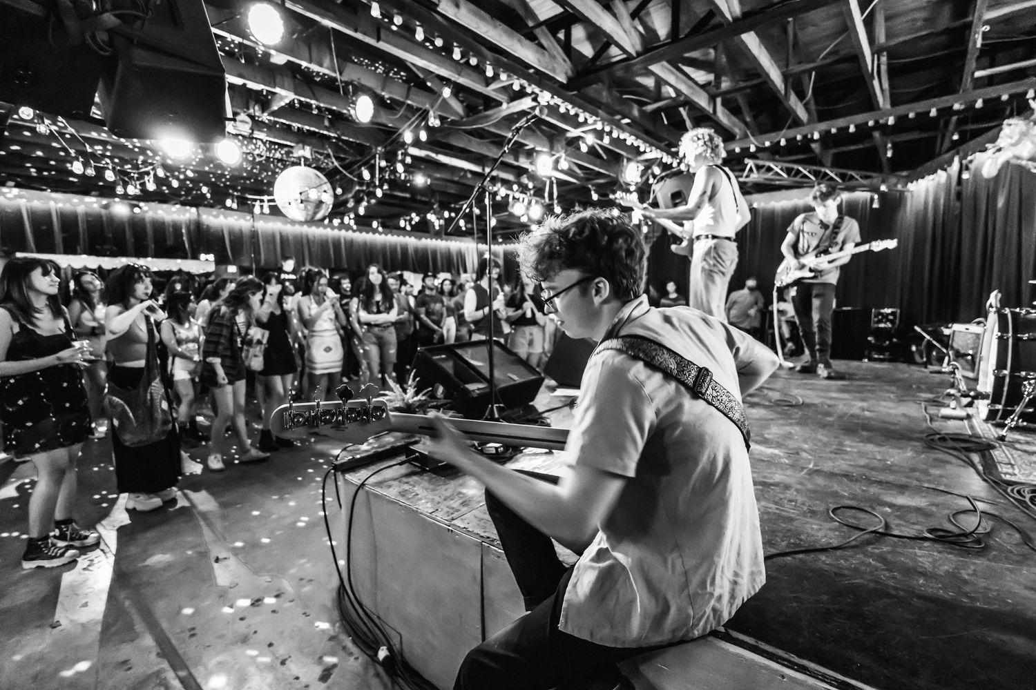 Musicians perform on stage at a lively concert venue with an energetic crowd.