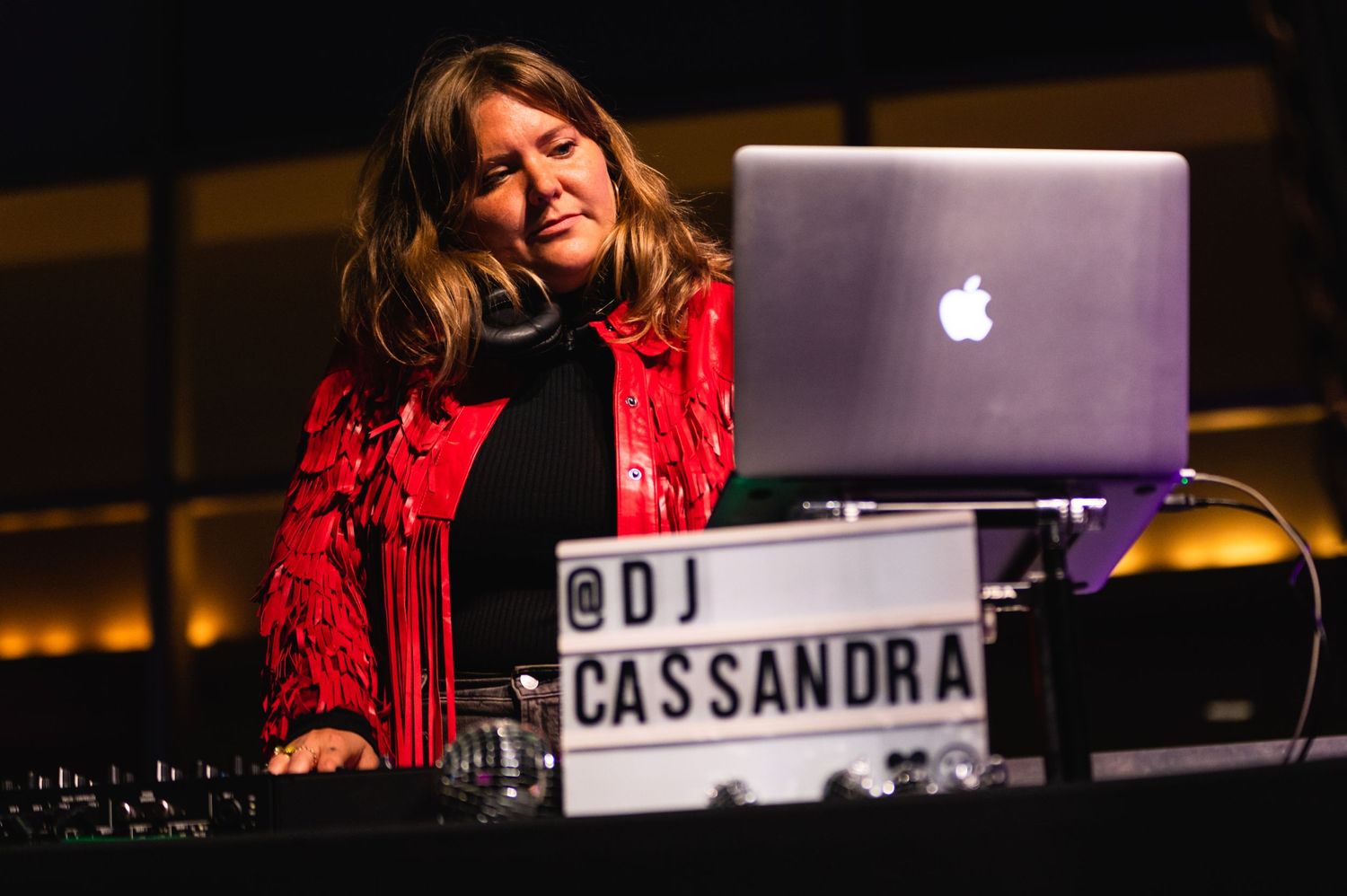 DJ performs with laptop at event console in dramatic lighting.