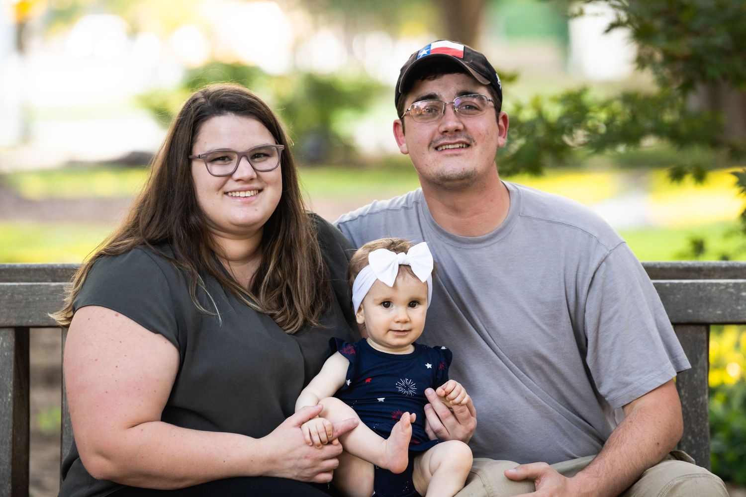 A family sits on a bench outdoors with their baby on a sunny day.