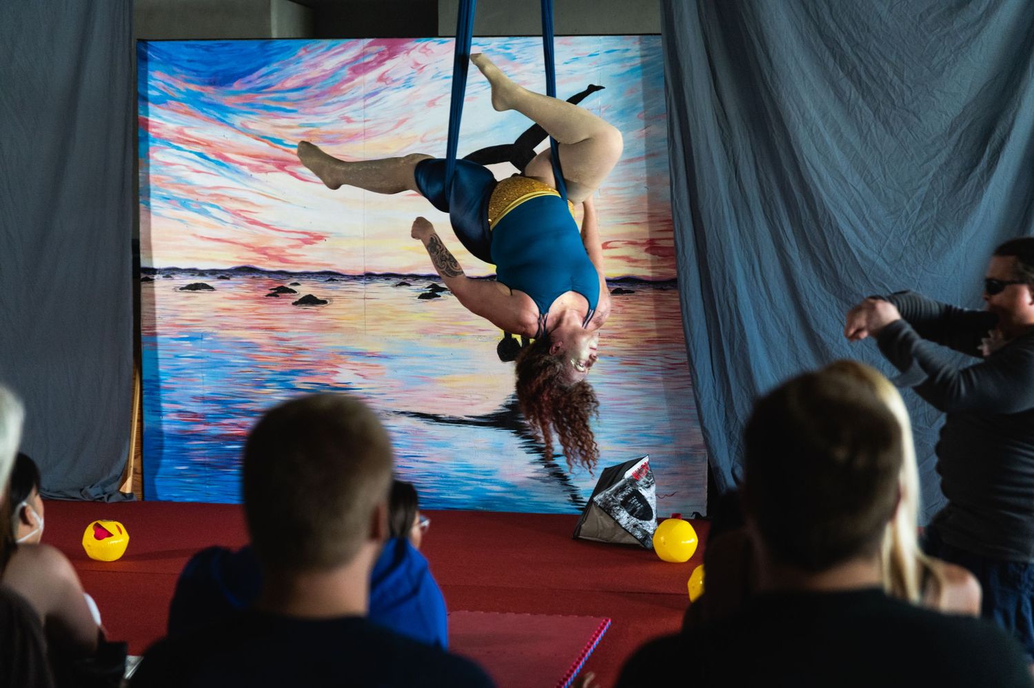 Aerial performance silhouetted against vibrant sunset backdrop with audience in foreground.
