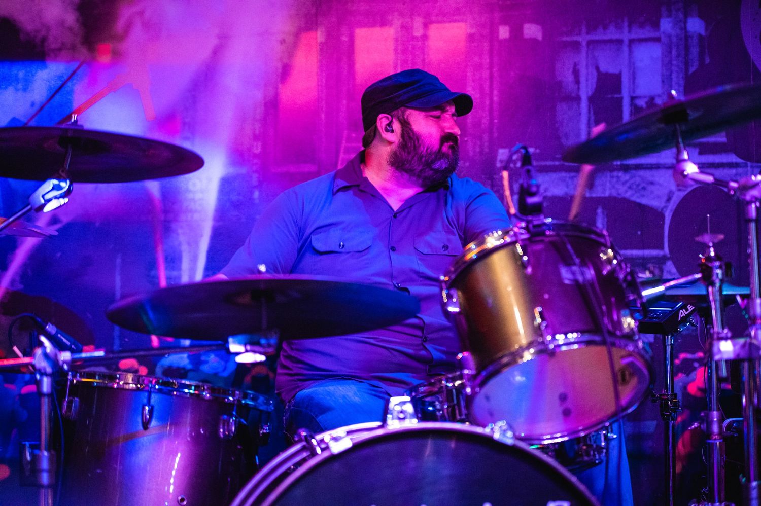 Drummer playing behind a drum kit illuminated by colorful stage lights.