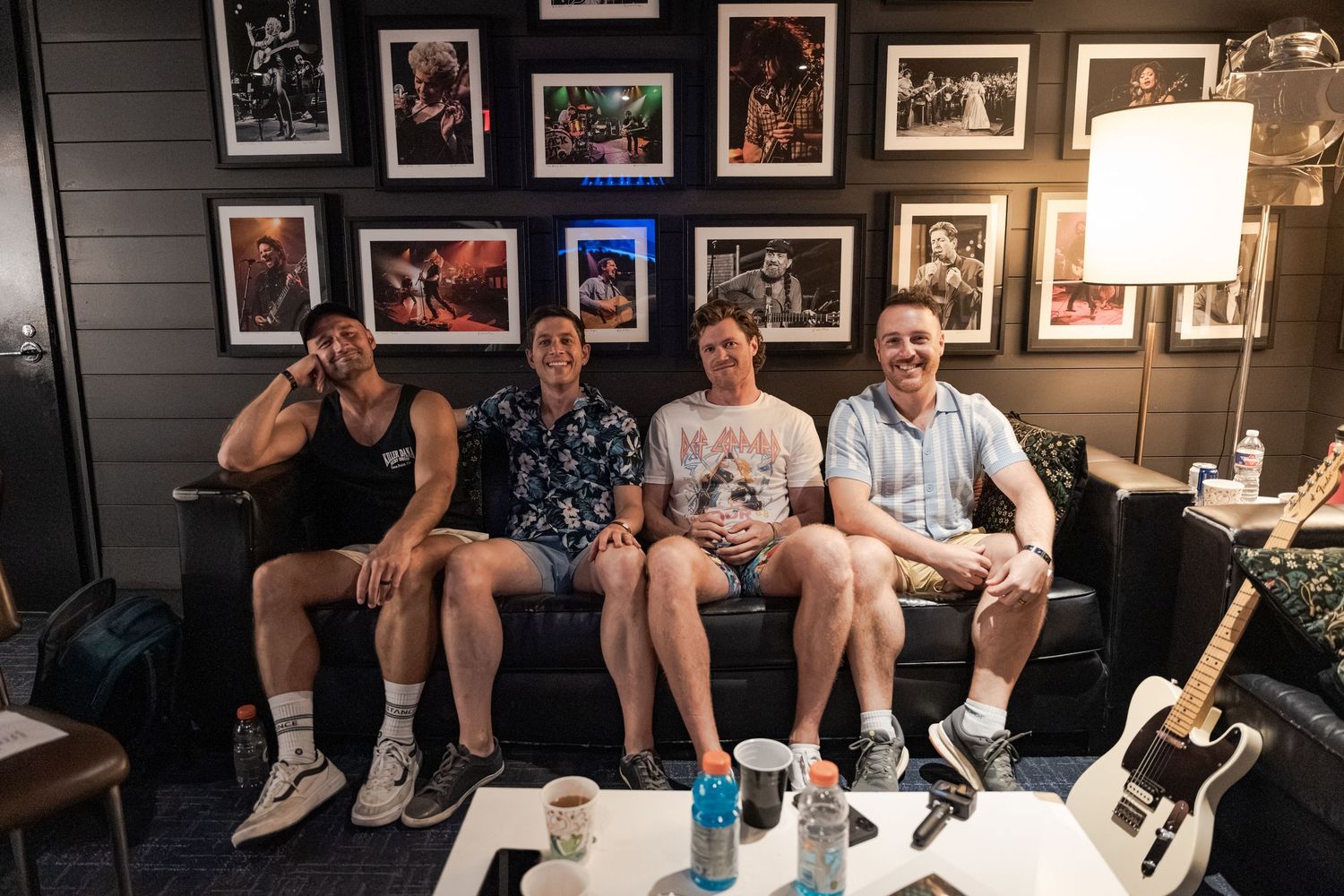 Four friends smiling together on a couch in a music-themed room with framed photos and a guitar nearby.