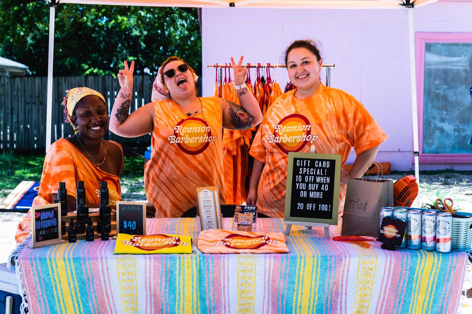 Food service workers in orange shirts prepare meals behind a colorful counter display at a restaurant.