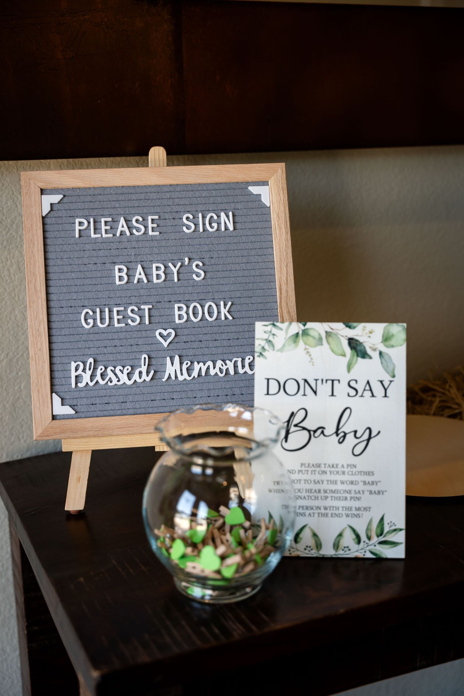 Gray letterboard sign asking guests to sign baby's guestbook displayed with a 'Don't Say Baby' sign and small floral vase.