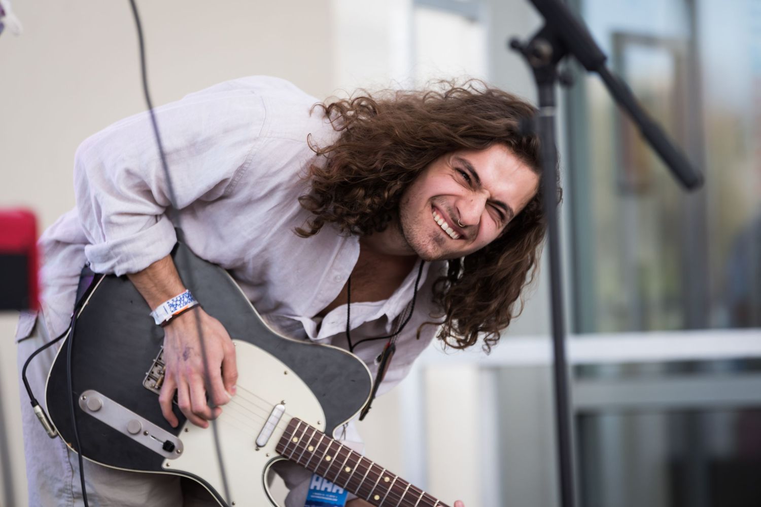 A guitarist performs on stage with curly hair and a grey shirt, playing with passionate energy and emotion.
