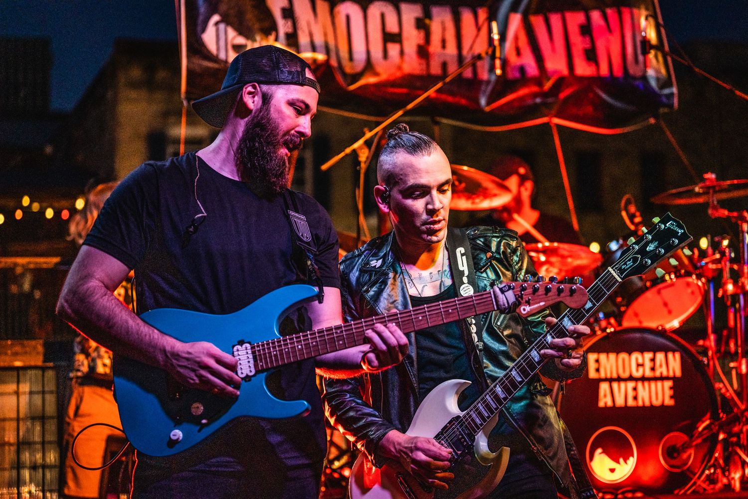 Musicians perform on stage with colorful red lighting and instruments during a live concert performance.