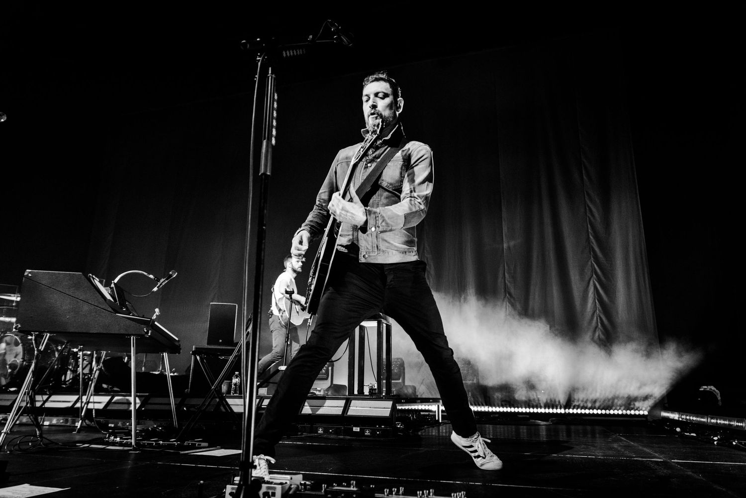 Black and white shot of a performer playing guitar on stage in energetic stance.