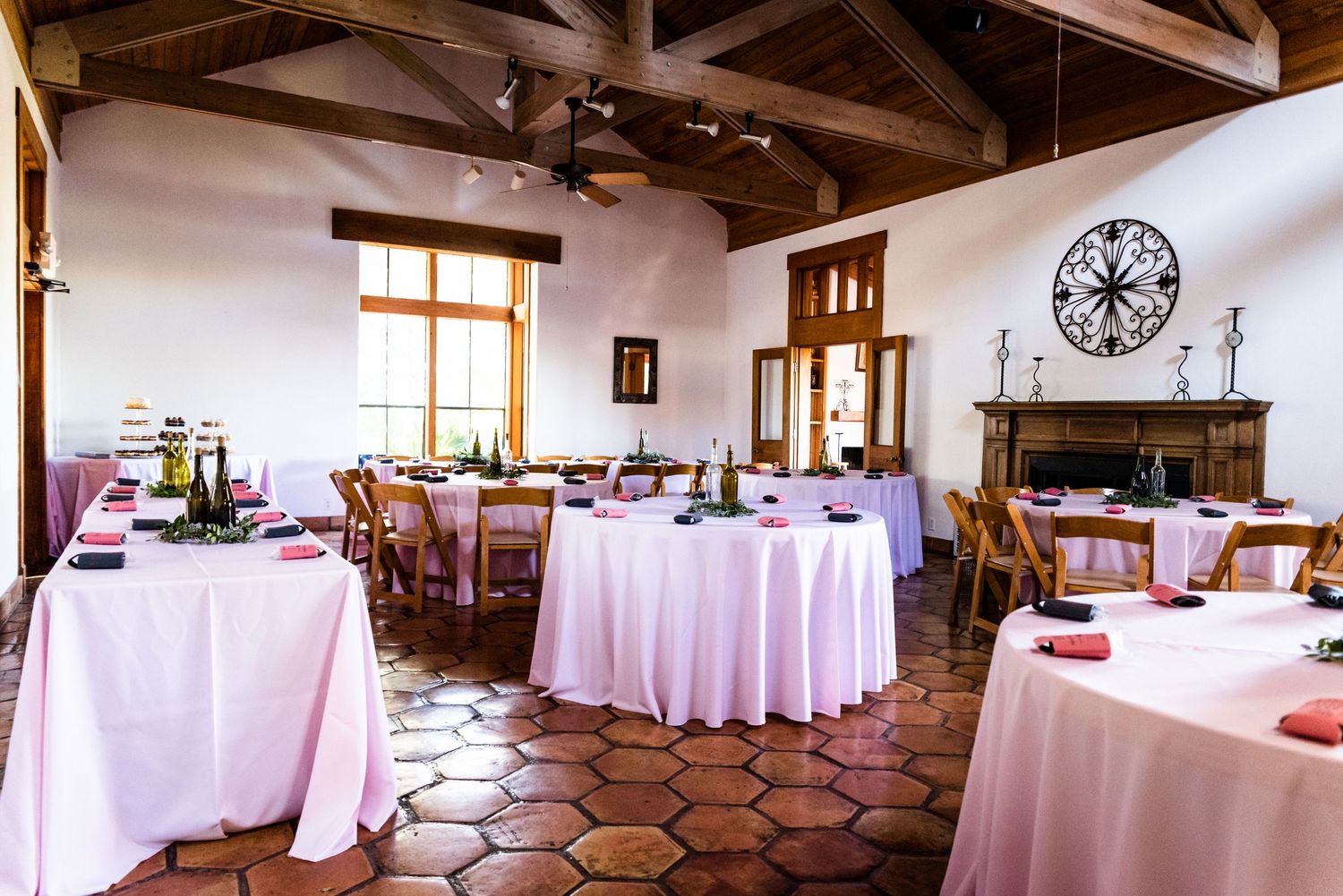 An elegant reception venue with round tables covered in white linens and wooden ceiling beams.