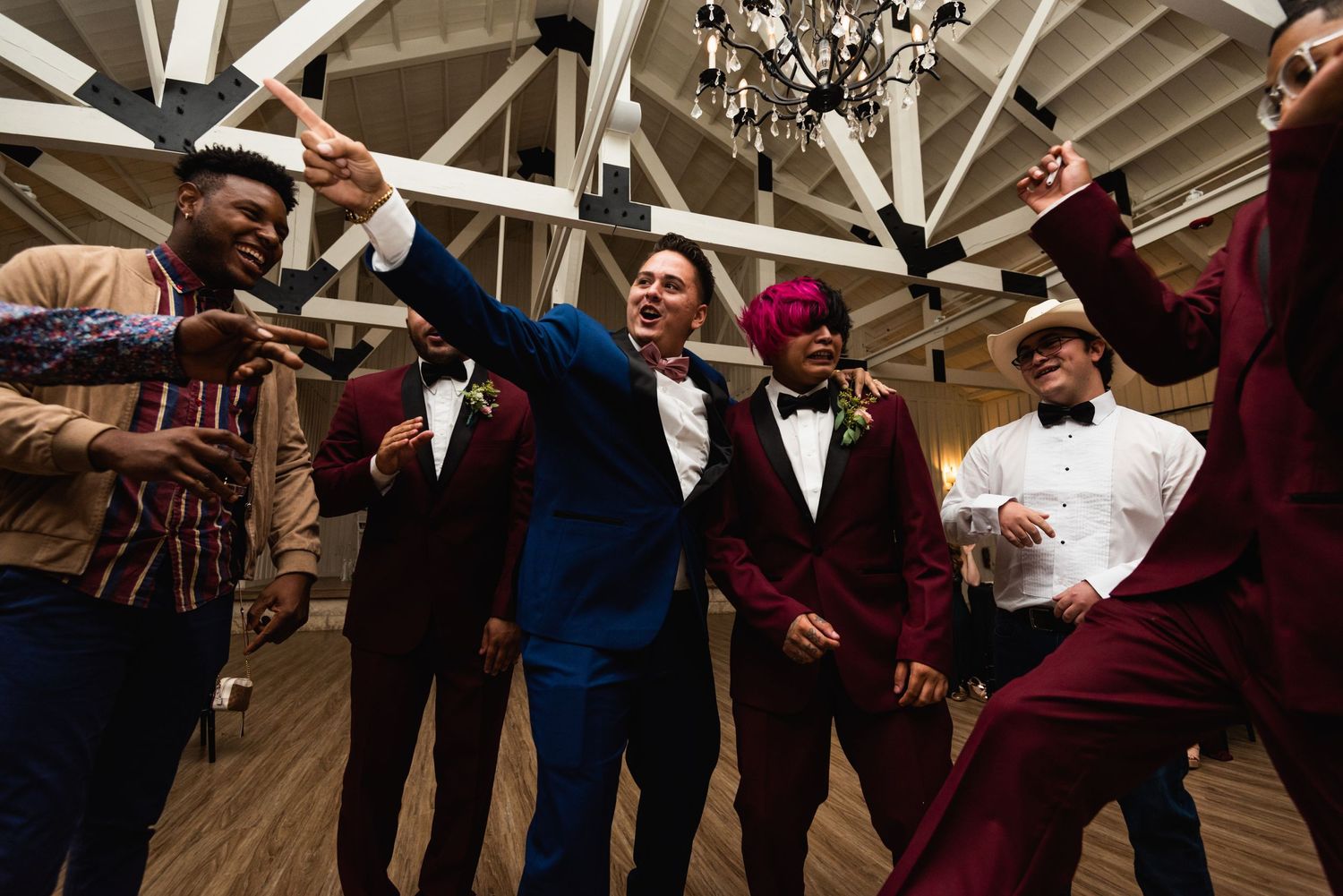 Group of wedding guests dancing and celebrating energetically under wooden beam ceiling.