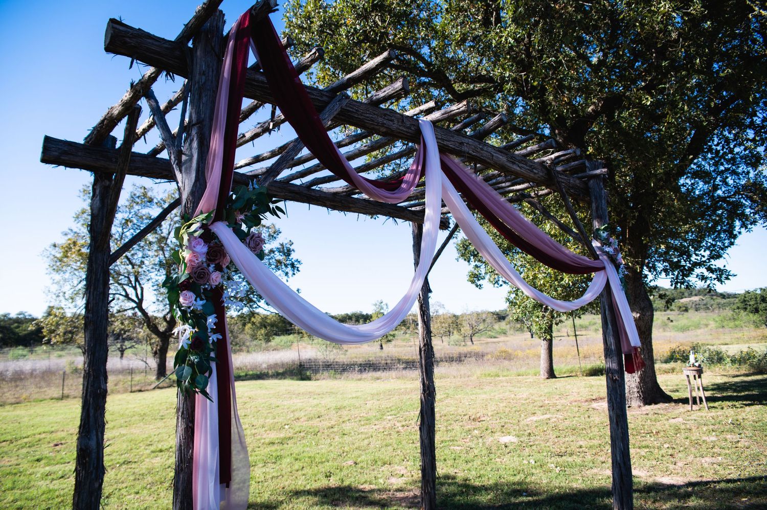Wooden pergola decorated with purple and white fabric draping for an outdoor wedding ceremony.