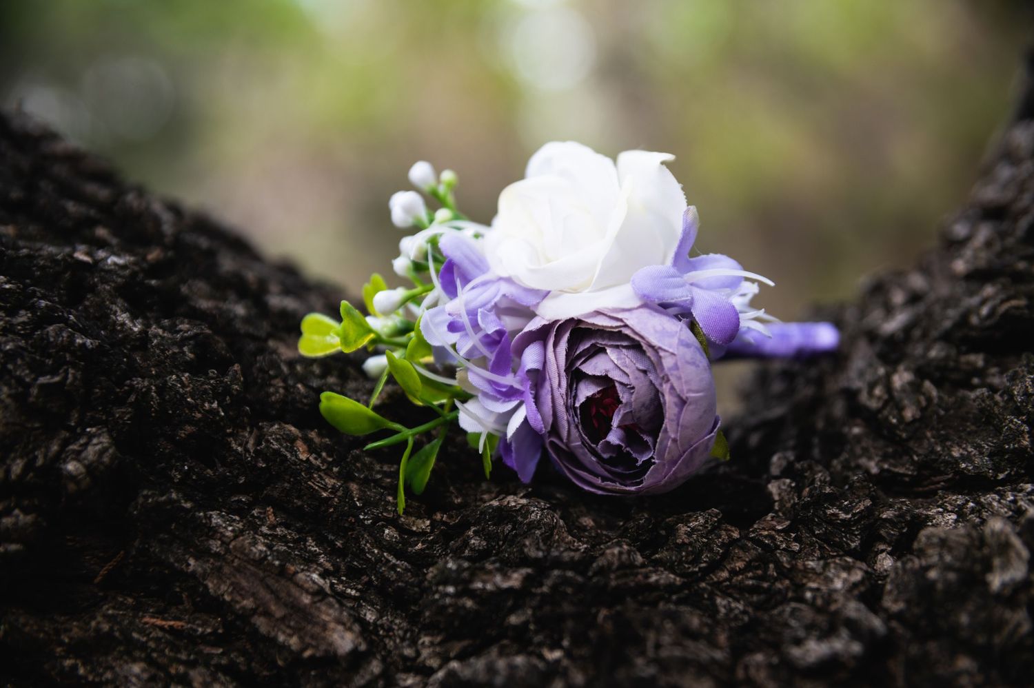 Purple and white roses with greenery arranged on dark tree bark.