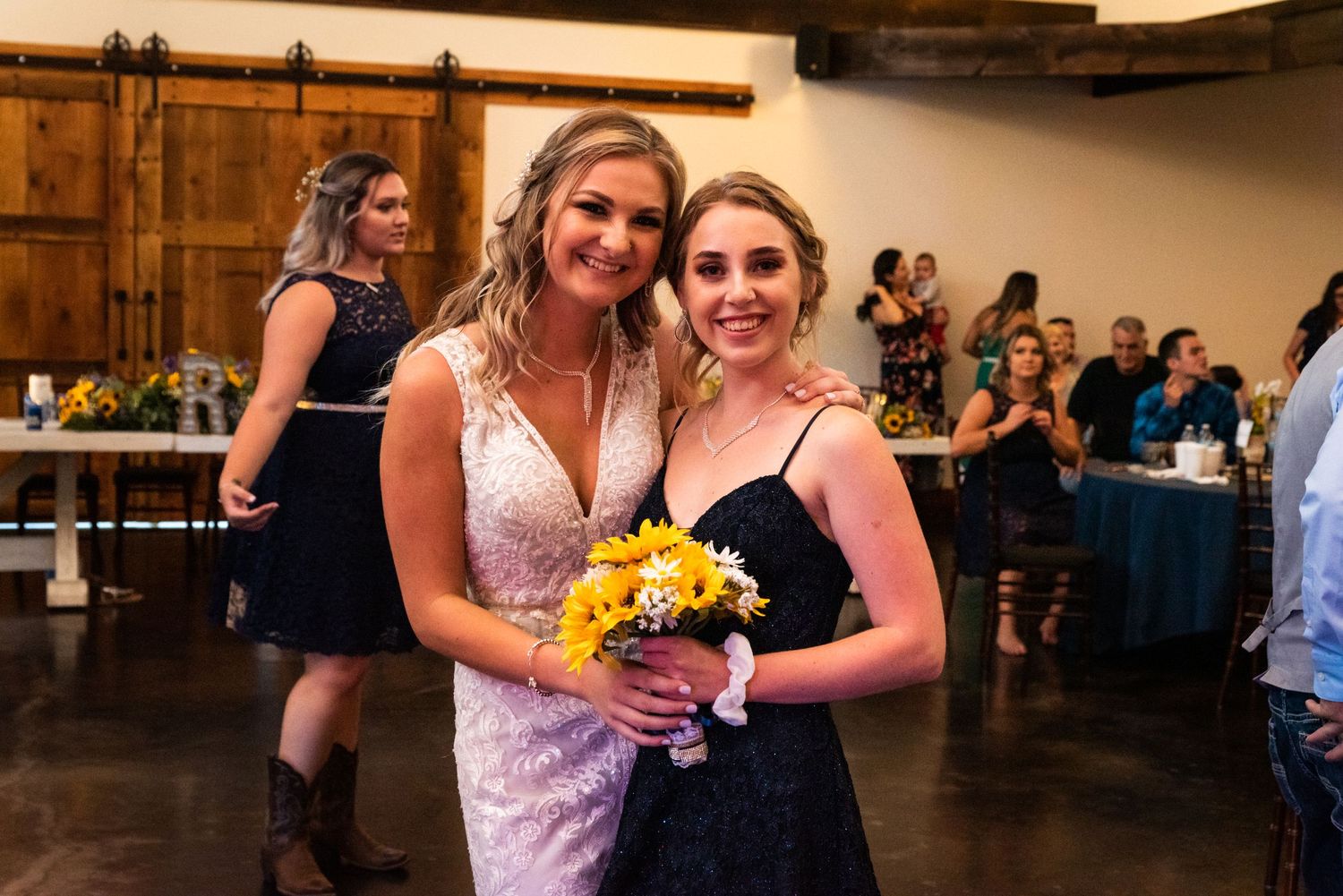 Wedding celebration with attendees holding yellow sunflower bouquet in rustic indoor venue.