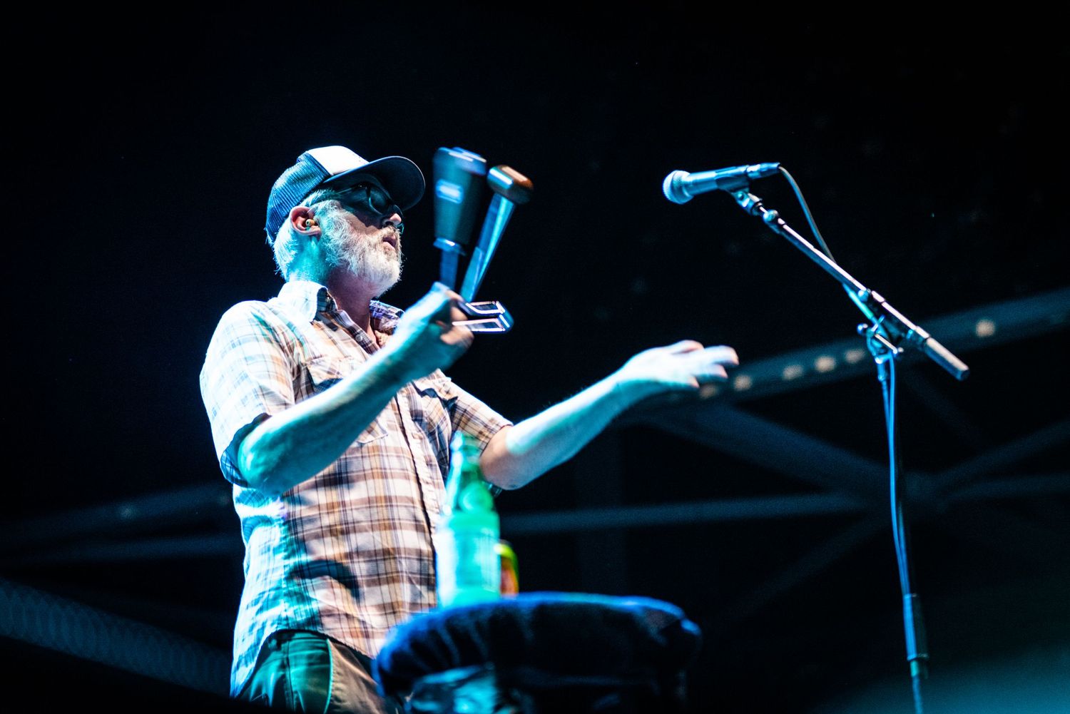 Musician performing with instruments under blue stage lighting with microphone setup.