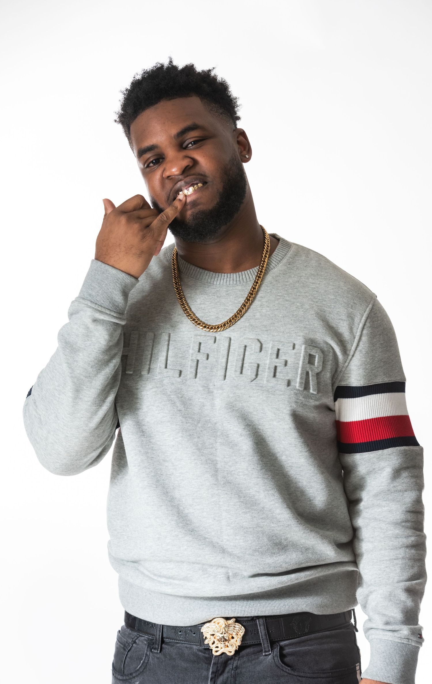 Casual portrait featuring gray designer sweatshirt with red and navy arm stripes and gold chain accessory.