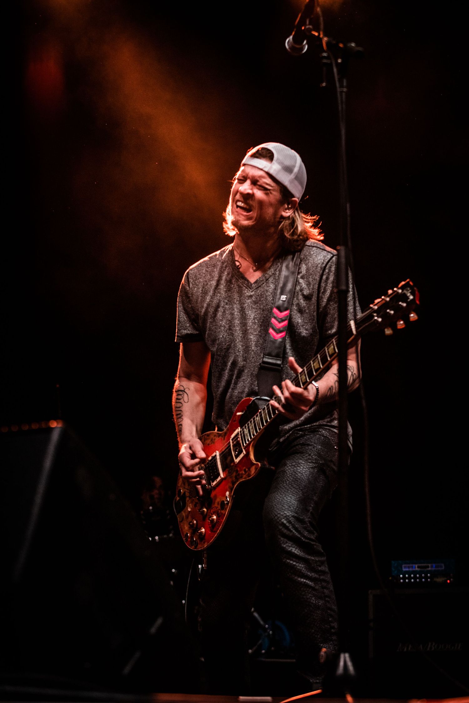 Musician in backwards cap plays red electric guitar during concert performance.