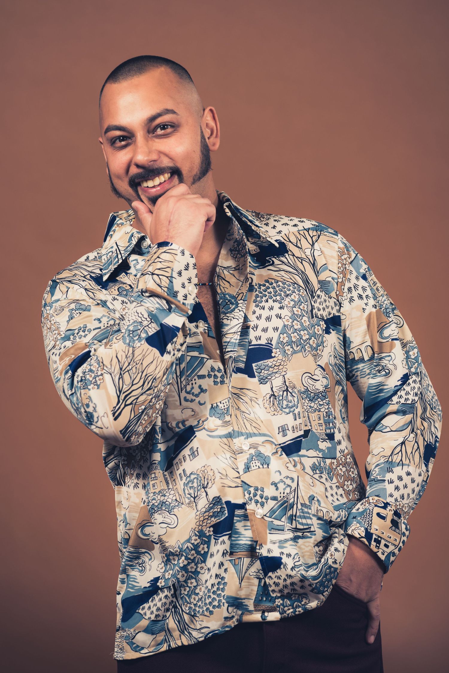 Portrait of person wearing patterned blue and white button-down shirt against brown background.