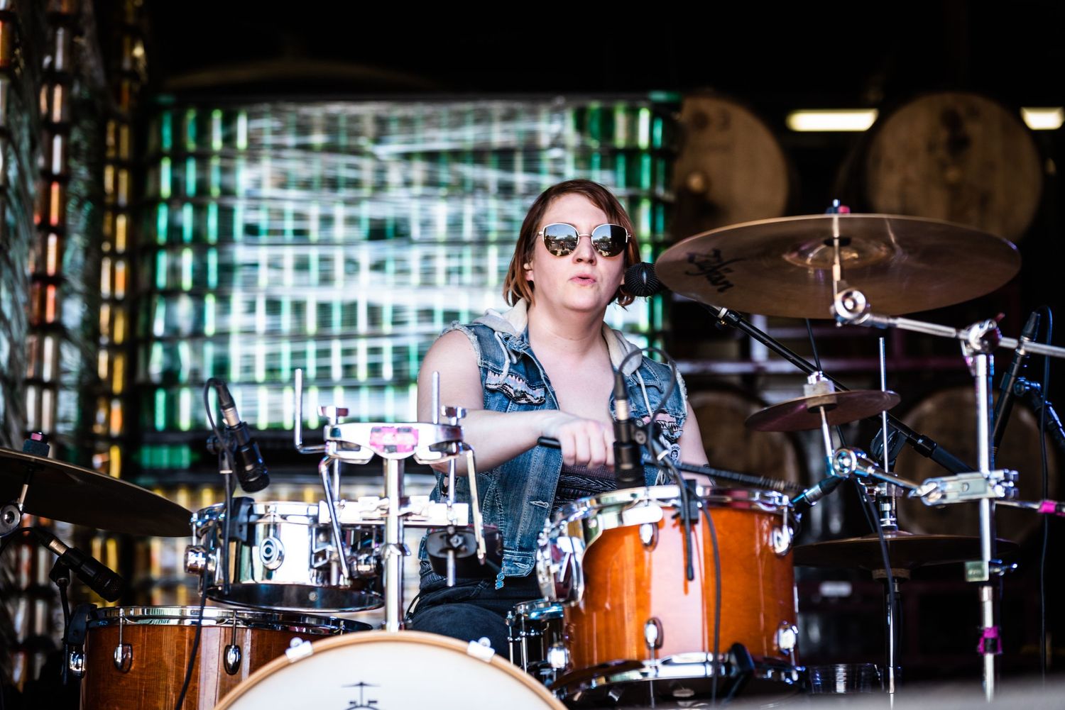 Drummer performs with focus behind orange drum kit under dramatic stage lighting.