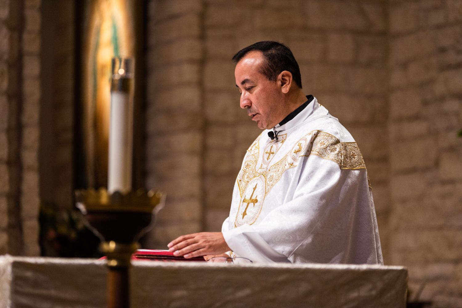 A priest in white vestments prepares for mass at a stone altar in church.