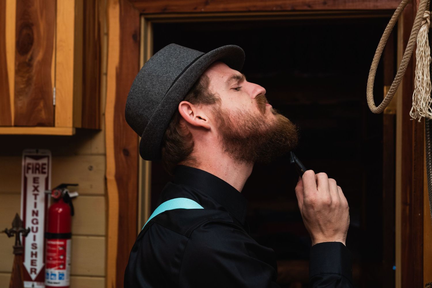 Person with beard wearing cap looks upward in rustic cabin setting.