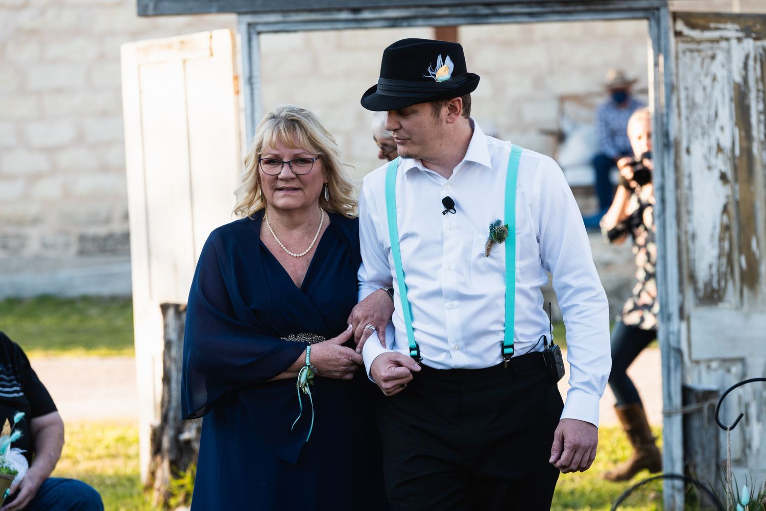 A formal couple walks together outside a stone building during an event.