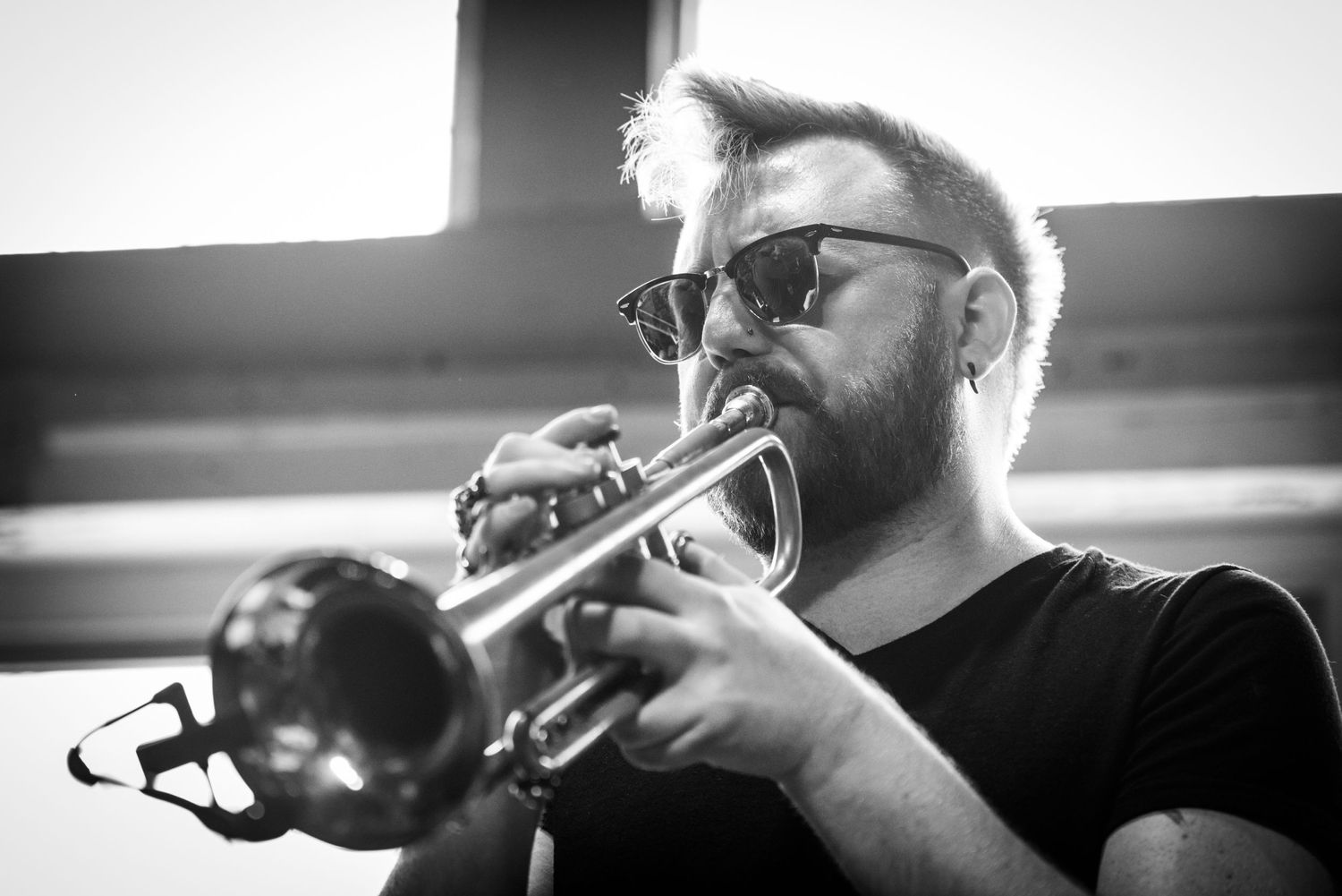 Close-up black and white photo of musician playing trumpet with intense focus and sunlit backlight.