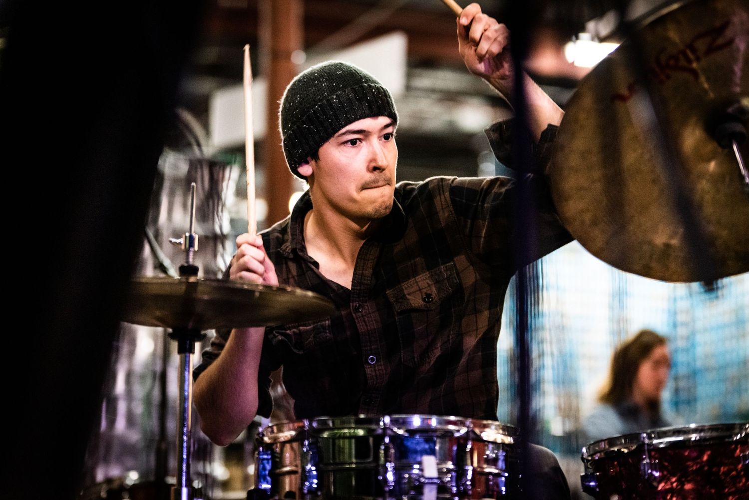Musician in beanie playing drums during energetic performance.